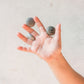 A small childs hand with fingers outstretched.  Small wooden stone pebbles are balanaced between the child's fingers.