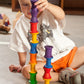 a small child plays with rainbow coloured wooden spools.  They are stacking the spools in two towers,