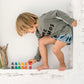 A small child engrossed in play. He is leaning over towards 6 small wooden people in rainbow colours