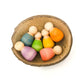 6 wooden babies nestled in a half coconut shell.  Each baby nin is painted a different rainbow colour.