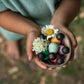 a small child holds a half cocont shell containing flowers and small wooden baby nins